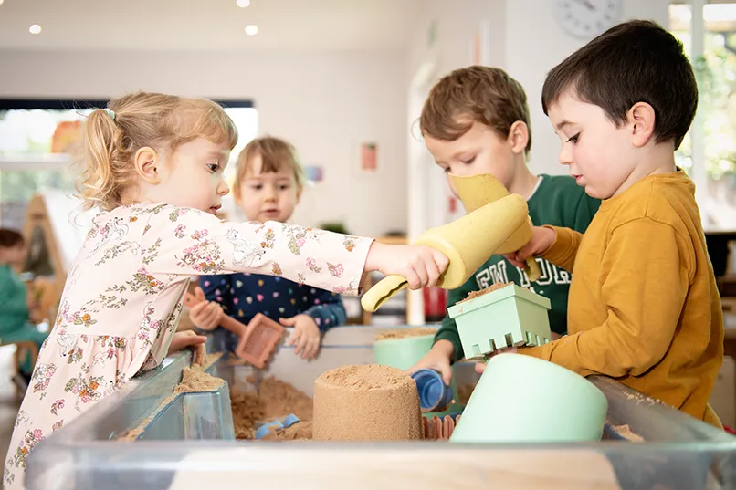 Children playing with sand toys at a sand table indoors.