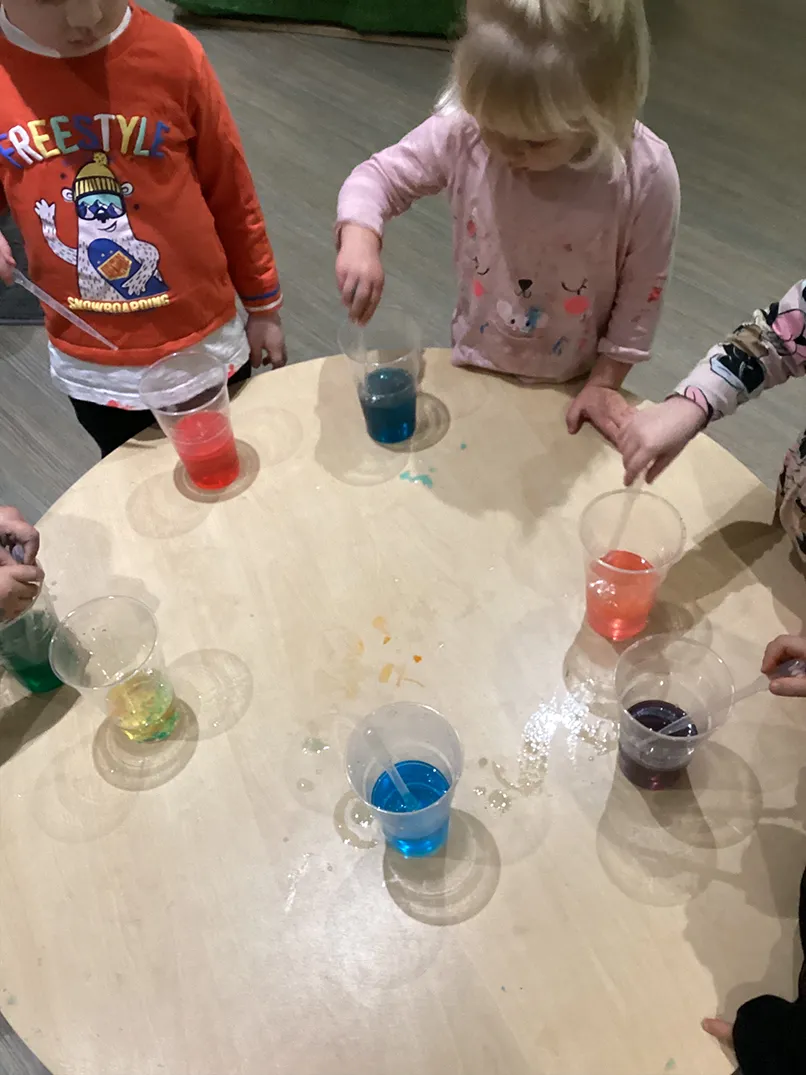 Children engaging in a colorful water play activity on a wooden table.