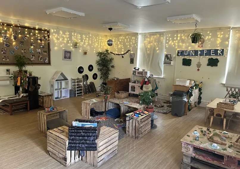 Cozy room decorated with fairy lights, rustic furniture, plants, and a sign spelling "JUNIPER."