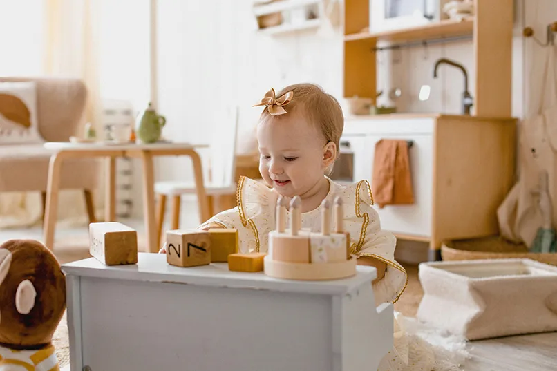 A toddler playing with wooden blocks in a sunlit room with cosy décor.