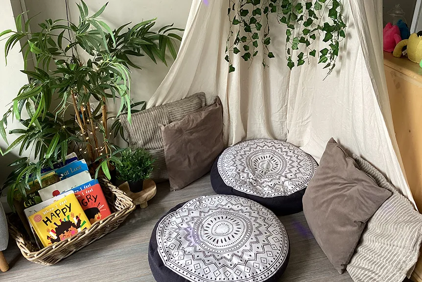 A cozy reading nook with cushions, a teepee, plants, and a basket of books.