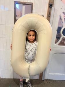 Child at the Chiswick House Day Nursery & Preschool celebrating the nursery's 'Good' Ofsted rating with an 'O' balloon.