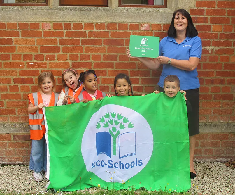 A group of children holds an Eco-Schools flag, celebrating their Green Flag Winner award for 2024, in front of a brick wall.