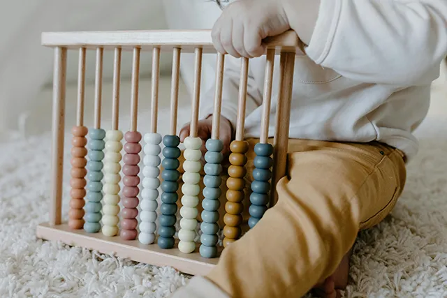 A child holds an abacus with colorful beads, seated on a soft rug, focused on exploring the educational toy.